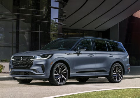 A gray 2025 Lincoln Aviator® SUV is parked outside a modern building showcasing the driver’s side of the vehicle. | Friendly Lincoln in Monroe MI