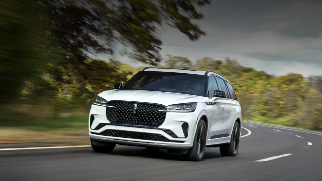 A white 2025 Lincoln Aviator® SUV is being driven down a road lined with trees. | Friendly Lincoln in Monroe MI
