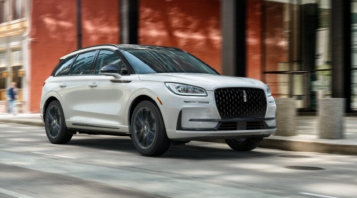 A white 2025 Lincoln Corsair® SUV with the Jet Appearance Package is being driven through a city.| Friendly Lincoln in Monroe MI
