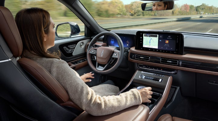 A 2026 Lincoln Aviator® SUV is being driven hands-free on a highway near a forest | Friendly Lincoln in Monroe MI