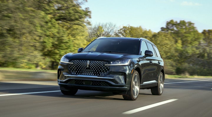 A 2026 Lincoln Black Label™ Aviator® SUV is being driven down a road lined with trees. | Friendly Lincoln in Monroe MI
