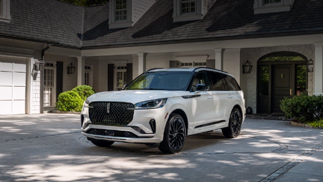 A white 2026 Lincoln Aviator® SUV is parked in the driveway of a luxury home. | Friendly Lincoln in Monroe MI