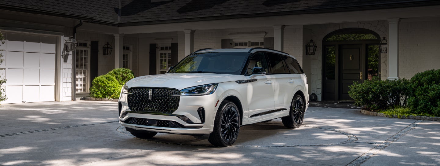 A white 2026 Lincoln Aviator® SUV is parked in the driveway of a luxury home. | Friendly Lincoln in Monroe MI