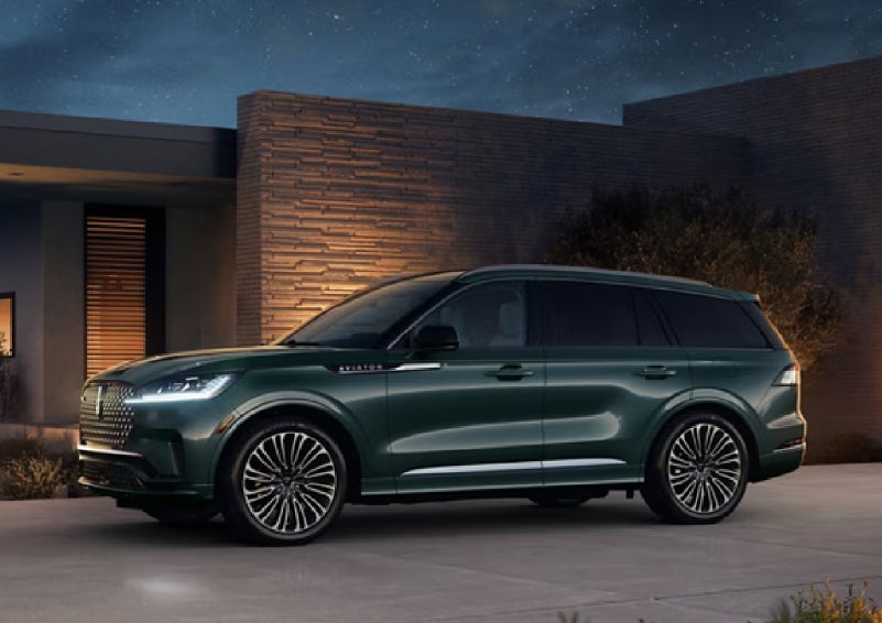 A green 2027 Lincoln Aviator® SUV is parked outside a contemporary home. | Friendly Lincoln in Monroe MI
