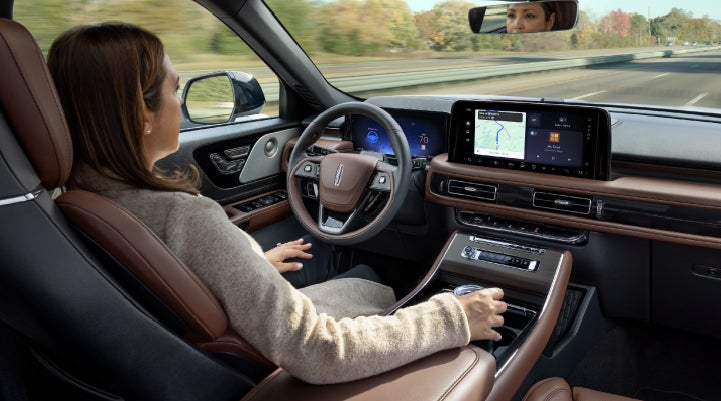 A 2027 Lincoln Aviator® SUV is being driven hands-free on a highway lined with trees. | Friendly Lincoln in Monroe MI