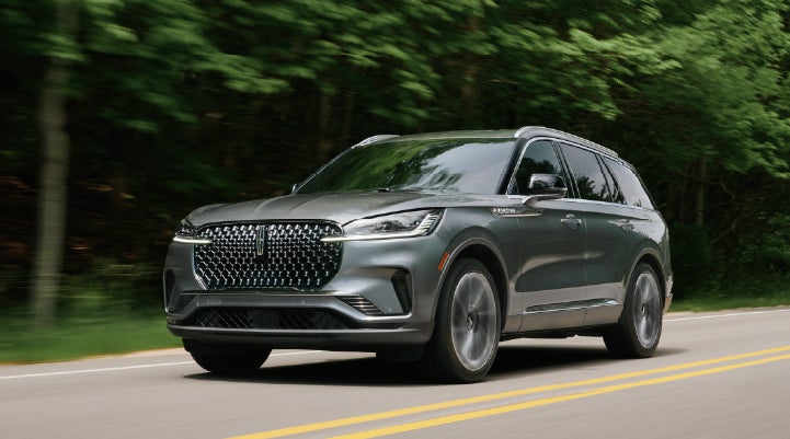 A 2027 Lincoln Aviator® SUV is being driven down a road lined with trees. | Friendly Lincoln in Monroe MI