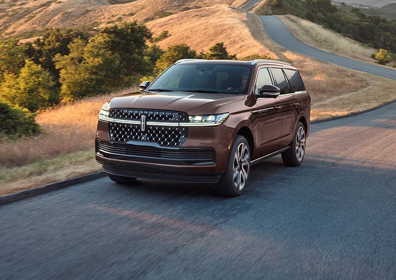 A 2027 Lincoln Navigator® Black Label™ SUV is being driven on a country road.