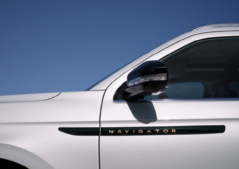 The side badge on the driver’s door of a 2027 Lincoln Navigator® Black Label™ SUV with Atmospheric Theme, features radiant copper-colored lettering.